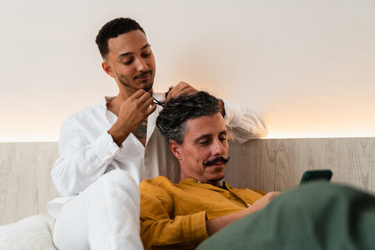 Young man styling hair of partner using smartphone in hotel room