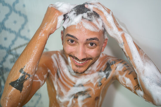 Smiling man washing hair with shampoo in shower