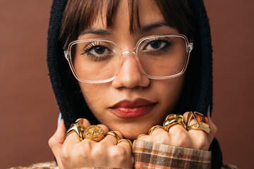 Woman wearing eyeglasses and several gold rings is posing