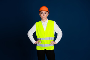 Confident female construction worker wearing safety gear, standing against a dark blue background.