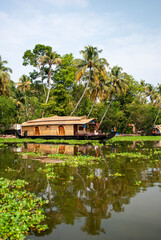 Houseboat on the backwaters of Kerala, India. Traditional wooden boat with thatched roof surrounded by lush greenery and tropical palm trees. Calm waters with reflection. Peaceful scenery.