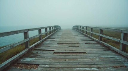 Obraz premium Foggy Wooden Bridge over Water Surrounded by Serene Landscape