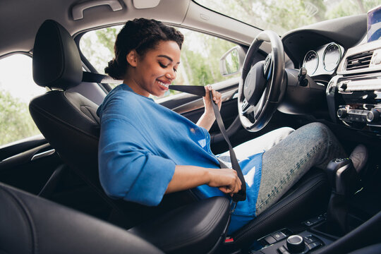 Young woman fastening seatbelt in modern car, smiling cheerfully. Captured in urban setting, reflecting safety and responsible driving.