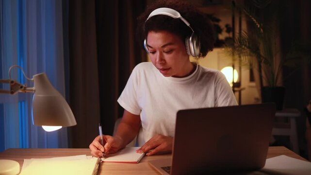 Pretty focused young woman preparing for exam studying at home workplace Busy female make notes while looking at laptop computer screen at late night Distance remote education
