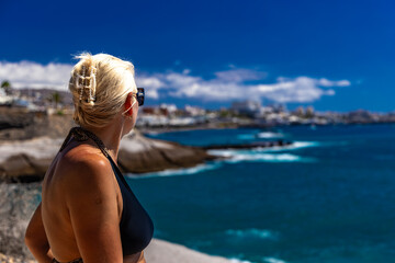Woman looks at the panorama of the Costa Adeje coast in Tenerife, a young girl in an elegant swimsuit relaxes on the Beach del Duque in Tenerife,