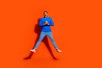 Young man in trendy blue polo jumps joyfully against vibrant orange backdrop