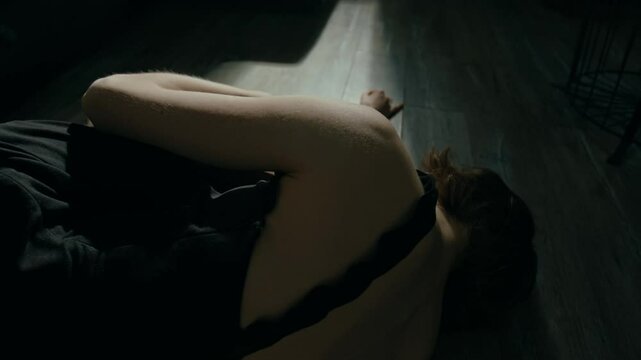 Unrecognisable exhausted young woman dressed in black chemise lying down on floor feeling down because of anxiety disorder