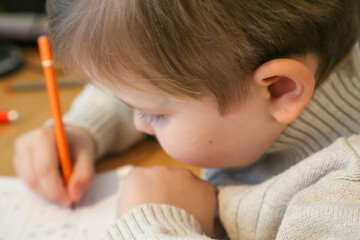A close-up shot of a young child deeply engaged in writing or solving a puzzle. The child, dressed...