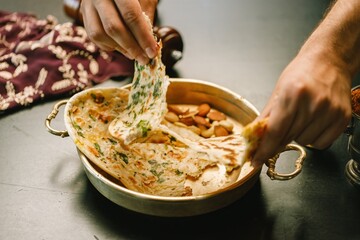 Hands gently pull apart a warm, herb-infused flatbread in an ornate brass bowl, surrounded by an assortment of nuts, evoking a festive atmosphere of traditional Indian dining