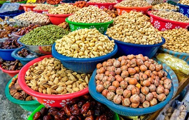 A stall at a market in Central Asia featuring a variety of nuts in colorful bowls. Cashews, pistachios, almonds, hazelnuts, pumpkin seeds, and dates.