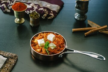 Warm spices and rich textures fill a copper pot of traditional Indian curry adorned with paneer cubes. Vibrant colors of herbs and spices surround it, creating a feast for the senses