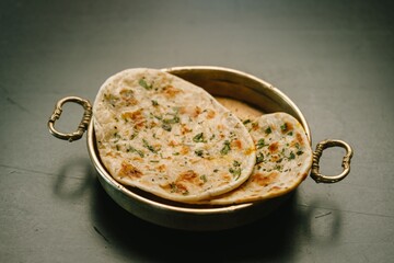 Warm, golden-brown stuffed parathas sit elegantly in a brass serving dish, showcasing the vibrant herbs and spices typical of traditional Indian cooking, made to perfection