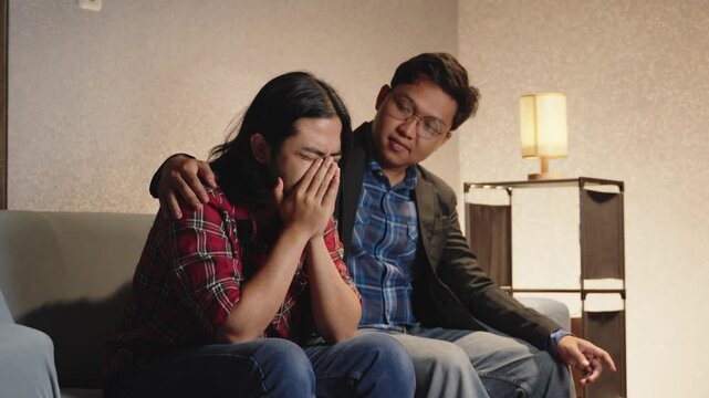 Best friend comforting stressed man sitting on sofa. Supporting a friend through emotional pain and mental health struggles. Emotional support, friendship, mental wellness, anxiety relief, depression
