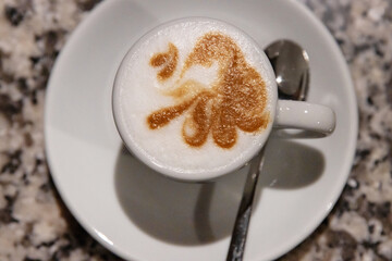 Top view of a cappuccino with intricate latte art in a white ceramic cup on a marble table, served with a spoon and sugar,  Coffee culture, creativity, barista skills concept and cozy cafe atmosphere 