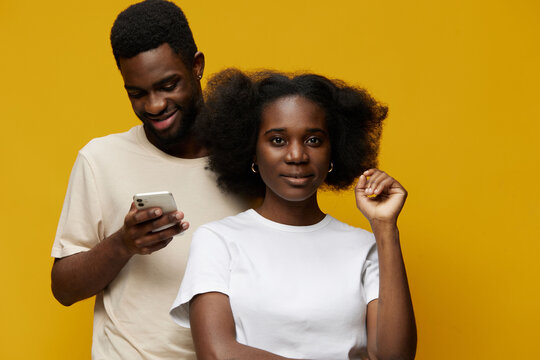 A young Black couple with natural hairstyles against a bright yellow background, showcasing confidence and modern fashion, embracing technology and connectivity