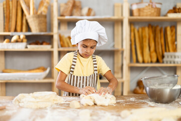 Girl training to works in bakery as baker, kneads dough, works with flour.