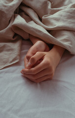 Hands rest gently under soft linen, capturing a quiet moment of warmth