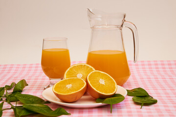 Freshly squeezed orange juice, refreshing and healthy, on a table with a pink and white checkered tablecloth, decorated with green leaves.