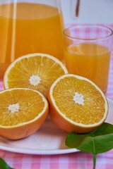 Freshly squeezed orange juice, refreshing and healthy, on a table with a pink and white checkered tablecloth, decorated with green leaves.