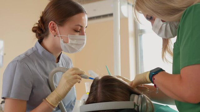Blonde Woman Dentist with Assistant Treat Teeth of Female Patient with Special Instrument. Treatment of Caries and Plaque in Dental Clinic. Concept of Medicine and Healthcare. Slow Motion.