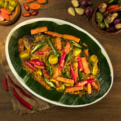 Indonesian traditional gurame pesmol, A colorful fish platter features fresh vegetables and spices arranged beautifully on a banana leaf in a cozy atmosphere