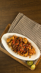 Indonesian traditional batagor, A beautifully arranged plate of chicken smothered in sauce sits on a striped napkin, complemented by fresh lime halves on a wooden surface