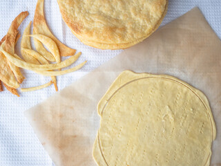 Cooking of a shortcrust puff pastry Napoleon cake with a pile of baked thin buttery layers, a raw layer rolled out on a baking paper and dough scraps on a white waffle towel.