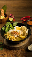 Indonesian traditional Laksa, Savory chicken soup with egg, fresh herbs, lime, and spices presented beautifully on a rustic wooden table, evoking warmth and comfort