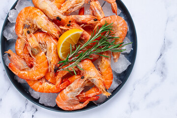 Freshly frozen shrimp on ice, with lemon and rosemary, on the marble table, top view, no people