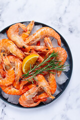 Freshly frozen shrimp on ice, with lemon and rosemary, on the marble table, top view, no people