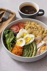 Bowl of couscous, meat, eggs and avocado and vegetables and cup of coffee