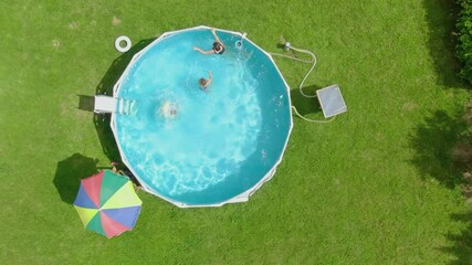 Aerial top view of the children swimming and jumping in the pool on the backyard on the green lawn. High quality 4k footage