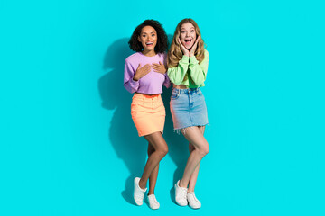 Two young women in colorful outfits on a vibrant turquoise background, expressing joy and...