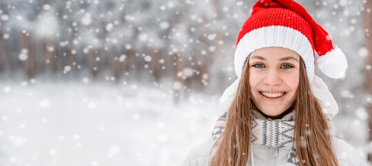Portrait of a beautiful young woman in a winter red hat smiling and playing with snow, picturesque winter forest