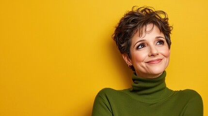 Close-up photo of a funny lady with a short hairdo, smiling with a good mood, looking slyly to the side, wearing a casual green warm turtleneck, isolated on yellow color background.