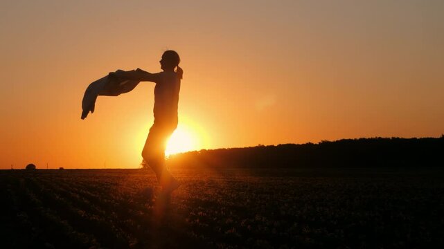 Silhouette of a middle-aged woman dancing in a rural field at sunset, playfully holding her jacket like a matador in a bullfight.