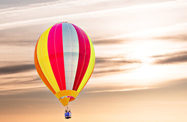 Colorful hot air balloon flying under orange sunset sky	