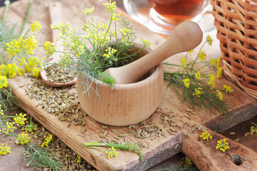 Fennel seeds in a mortar on wooden background with fresh flowers nearby, copy space, natural medicine, drink for breast milk production, sleep and stress care tea concept