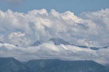 Russia. The Republic of Buryatia. Scenic view of the peaks of the Eastern Sayan mountain range drowning in fog and cumulus clouds from the valley of the Irkut River.