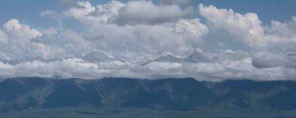 Russia. The Republic of Buryatia. Scenic view of the peaks of the Eastern Sayan mountain range drowning in fog and cumulus clouds from the valley of the Irkut River.