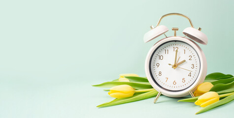 Alarm clock with yellow tulip flowers, switch to daylight saving time in spring, summer time...