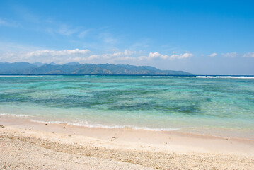 A beautiful beach scene with crystal-clear turquoise water and a pristine shoreline. The calm ocean and stunning mountains in the background create a peaceful, tropical paradise ideal for relaxation.