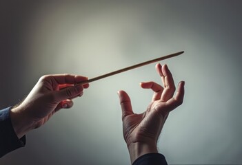 Two hands gracefully interact with a slender wand, poised in a moment of enchantment against a softly illuminated backdrop. The delicate interplay of fingers and the wand evokes a sense of wonder, as