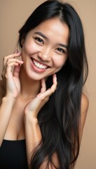 Fototapeta premium A beautiful young woman with long, flowing black hair beams with joy, her hands gently framing her face against a soft beige background. Her bright smile radiates positivity and warmth, inviting