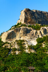 Majestic rock formation towers over lush green hills in bright daylight