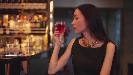 Sitting beautiful drinking alone in Cosmopolitan red cocktail waiting friends or couple at bokeh lighting luxurious beverage counter nightclub at pub and restaurant on Friday meeting night. Vinosity.