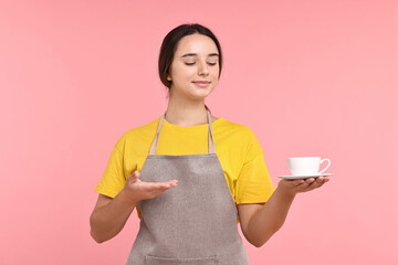 Girl in apron with cup of coffee on pink background. Work for teenagers