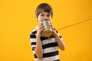 Boy using tin can telephone on yellow background