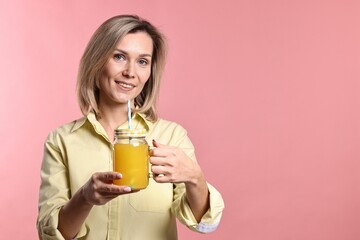 Woman with mason jar of orange juice on pink background. Refreshing drink