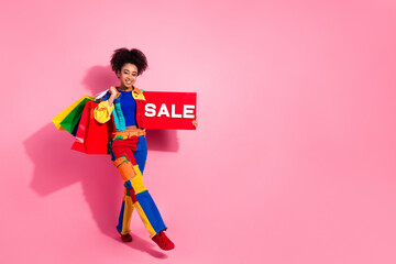 Colorful stylish woman holding sale sign and shopping bags against a pink background